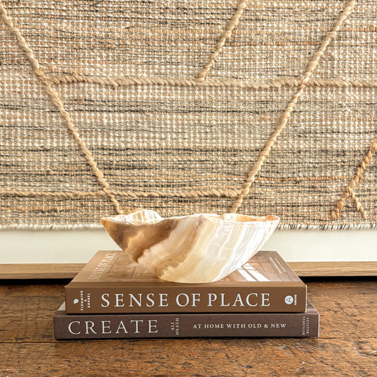 Small handcrafted onyx bowl styled on a wood table with textured wall art behind it