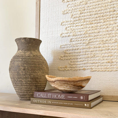 Small hand carved amber onyx bowl with soft natural veining displayed on stacked design books