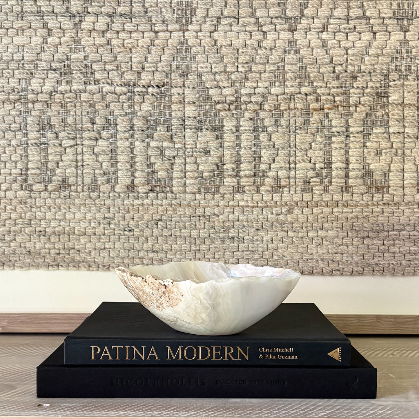 White and grey decorative stone bowl on a black book titled 'Patina Modern' against a textured wall.