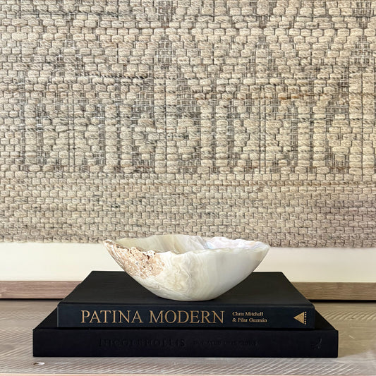 White and grey decorative stone bowl on a black book titled 'Patina Modern' against a textured wall.