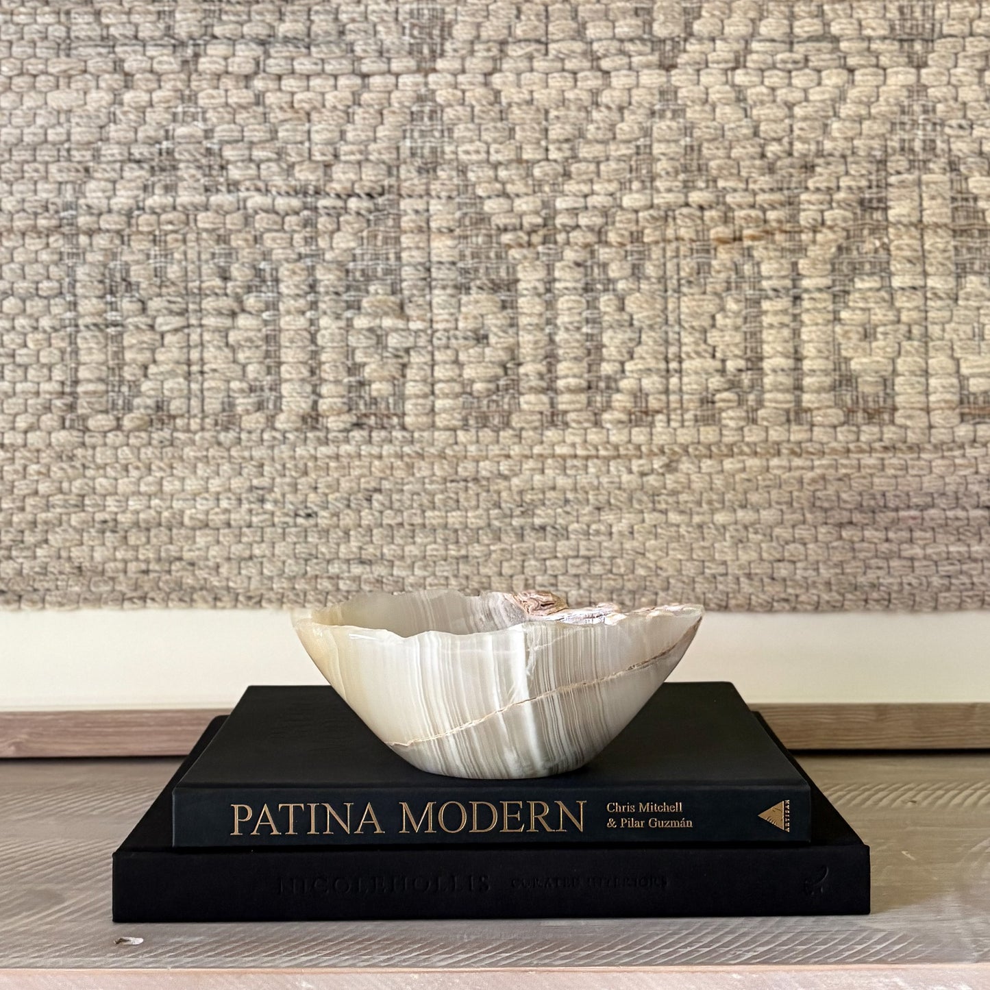 Decorative grey and white natural stone bowl on a book titled 'Patina Modern' with textured wall in the background