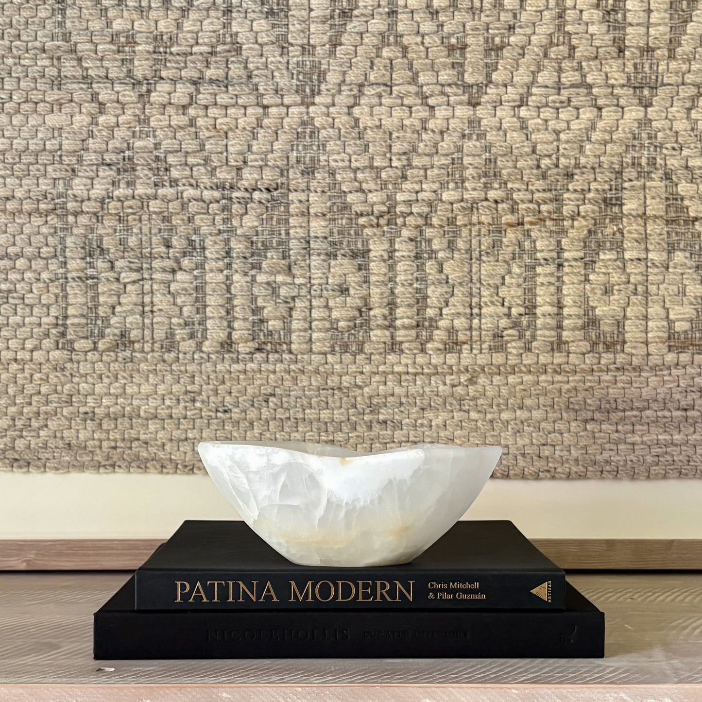 decorative white stone bowl on a black book titled 'Patina Modern' against a textured beige wall.