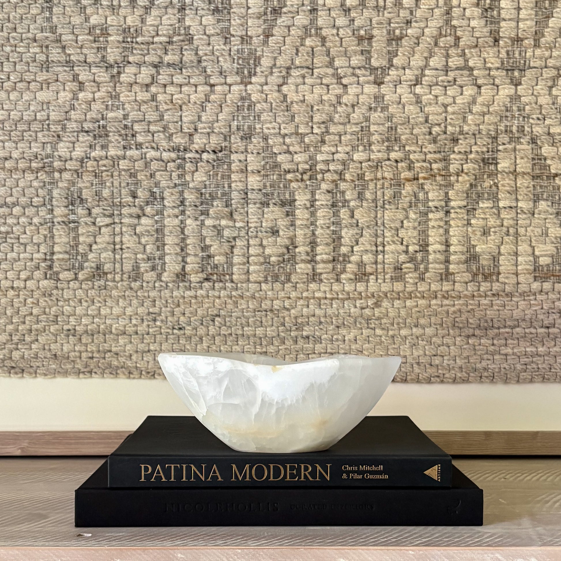 decorative white stone bowl on a black book titled 'Patina Modern' against a textured beige wall.