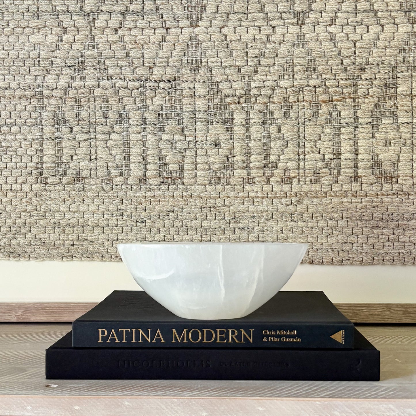 decorative White stone bowl on a black book titled 'Patina Modern' against a textured wall.