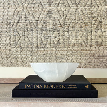 decorative White stone bowl on a black book titled 'Patina Modern' against a textured wall.