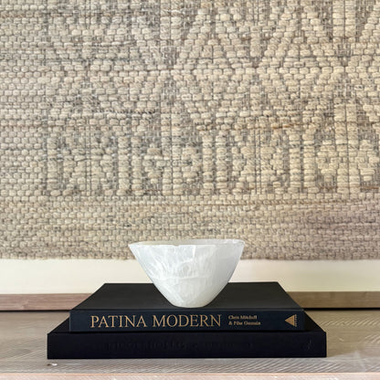 White natural stone bowl on black books with a textured beige wall in the background