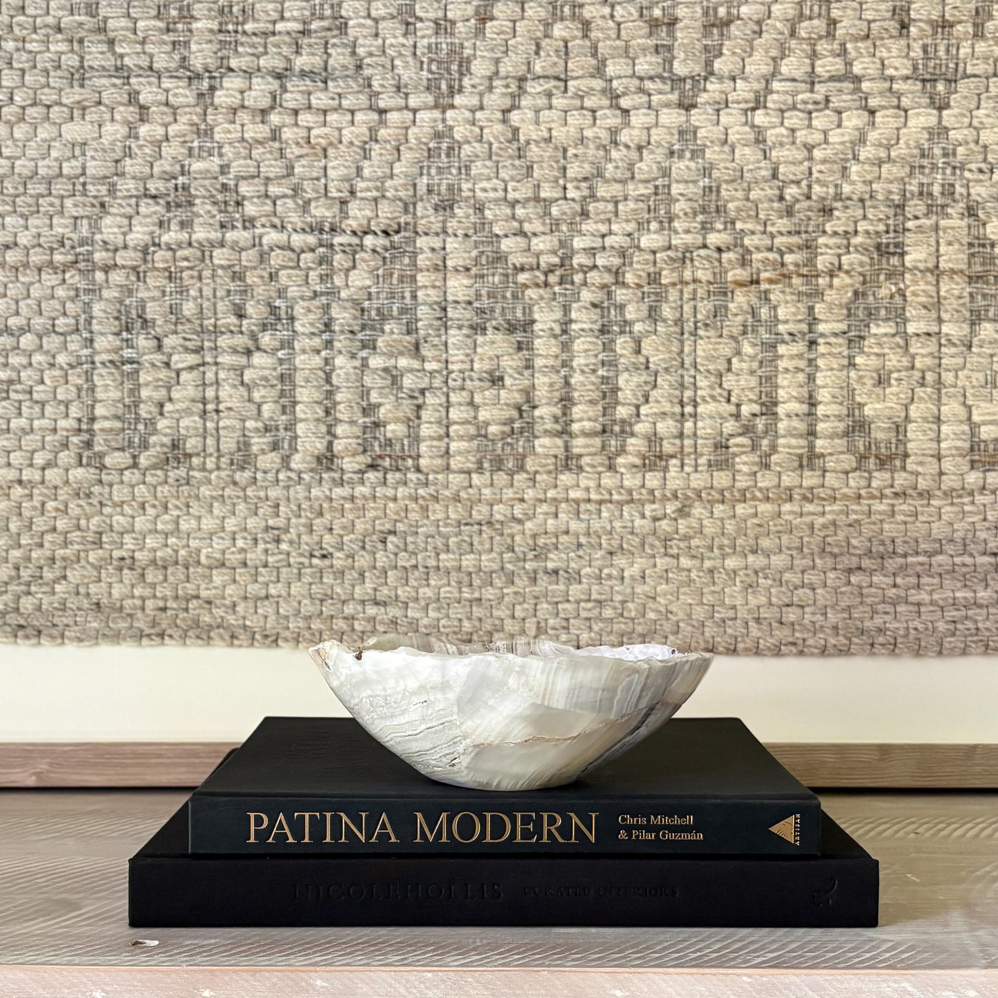 Decorative grey stone bowl on a book titled 'Patina Modern' against a textured wall.