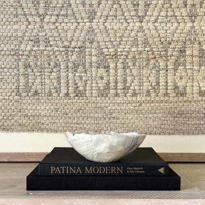 Decorative grey stone bowl on a book titled 'Patina Modern' against a textured wall.