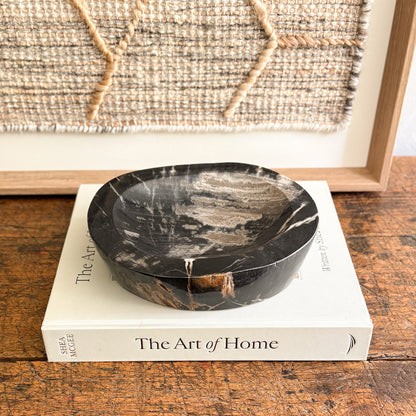 Black fossilized wood bowl on a book titled 'The Art of Home' with a woven wall art in the background.