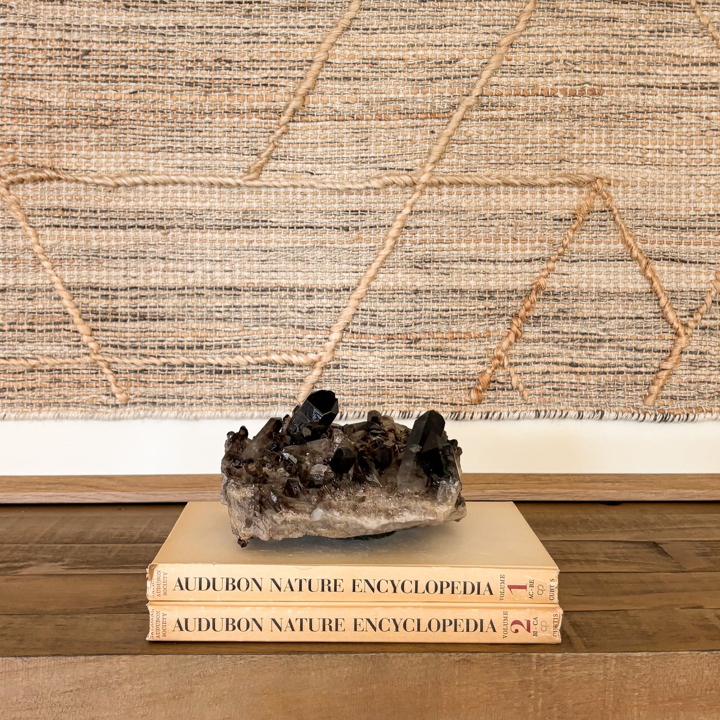 Large smoky quartz crystal cluster centerpiece displayed on stacked books for interior styling.