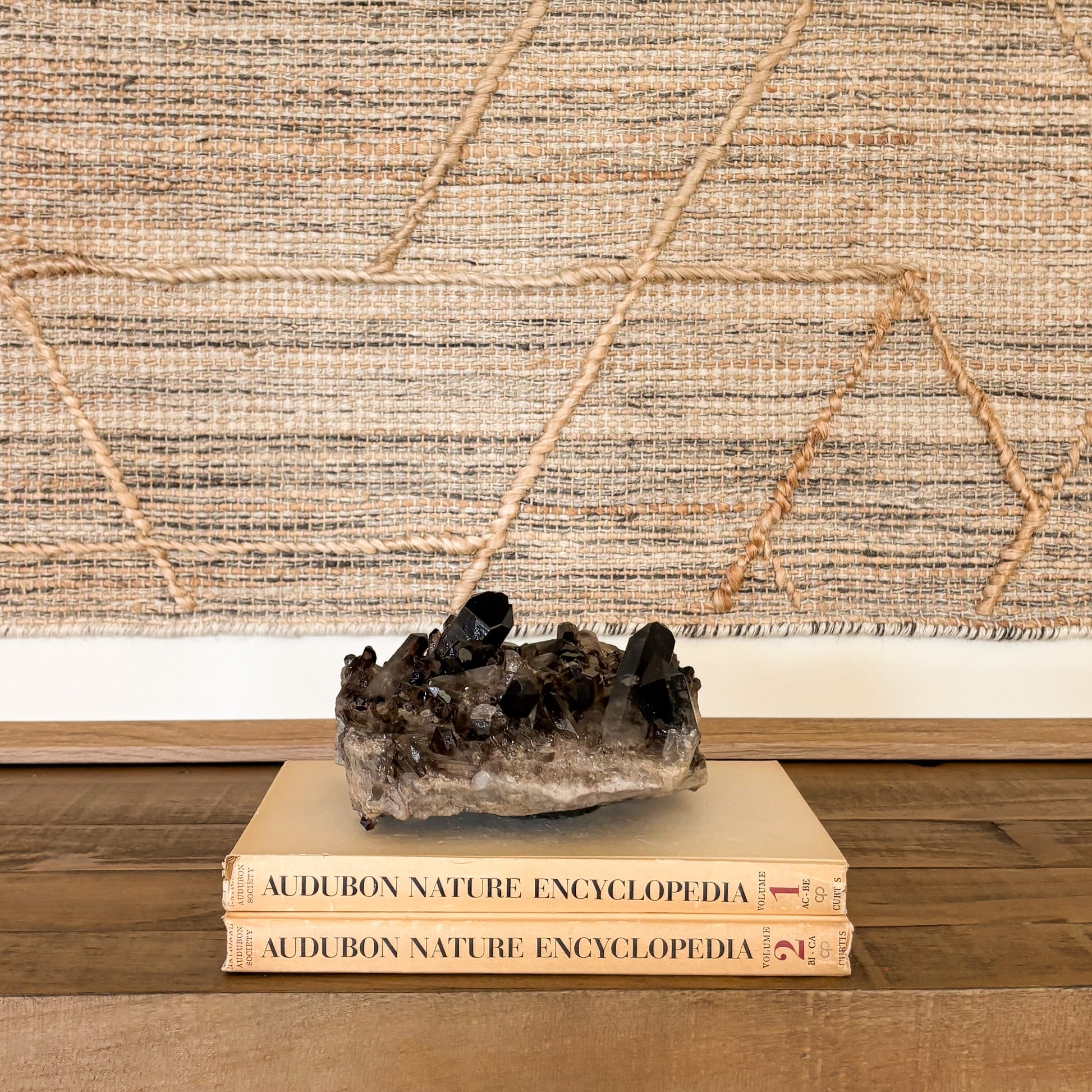 Large smoky quartz crystal cluster centerpiece displayed on stacked books for interior styling.