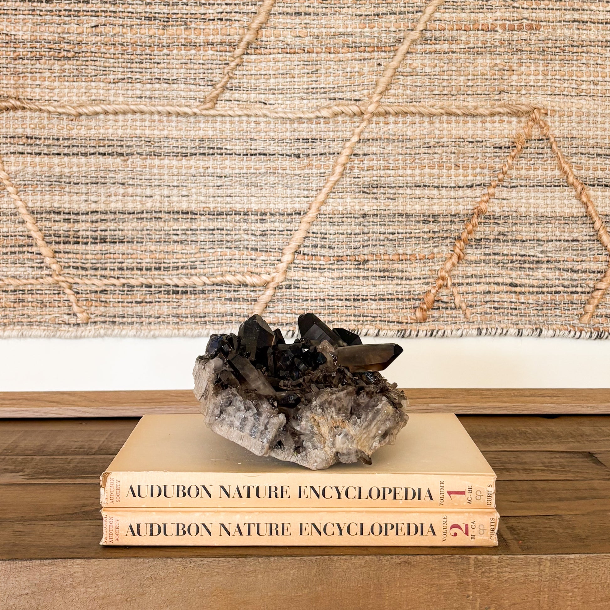 Smoky quartz crystal cluster mineral decor piece styled with vintage books and textile wall art.