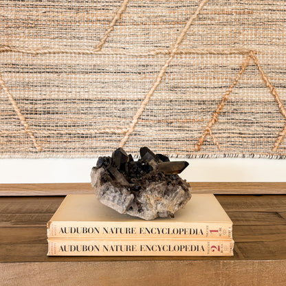 Smoky quartz crystal cluster mineral decor piece styled with vintage books and textile wall art.