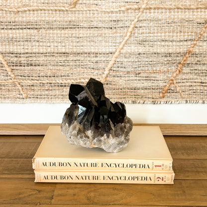 Smoky quartz crystal cluster styled on stacked books for earthy modern home decor