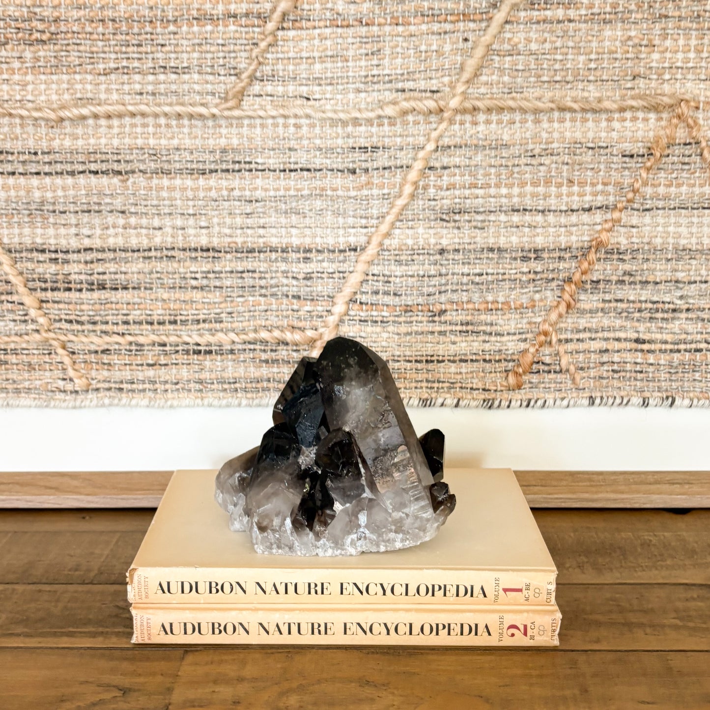 Dark smoky quartz crystal cluster decorative stone displayed on books on a wooden shelf.