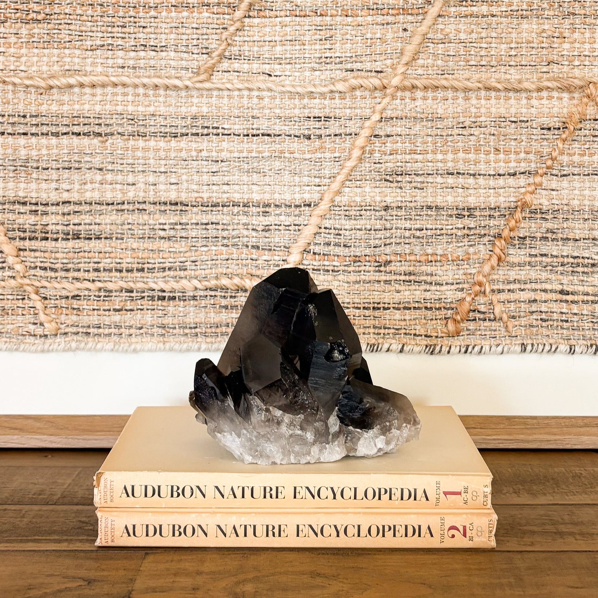Raw smoky quartz crystal cluster mineral specimen styled on stacked books in a boho home interior.