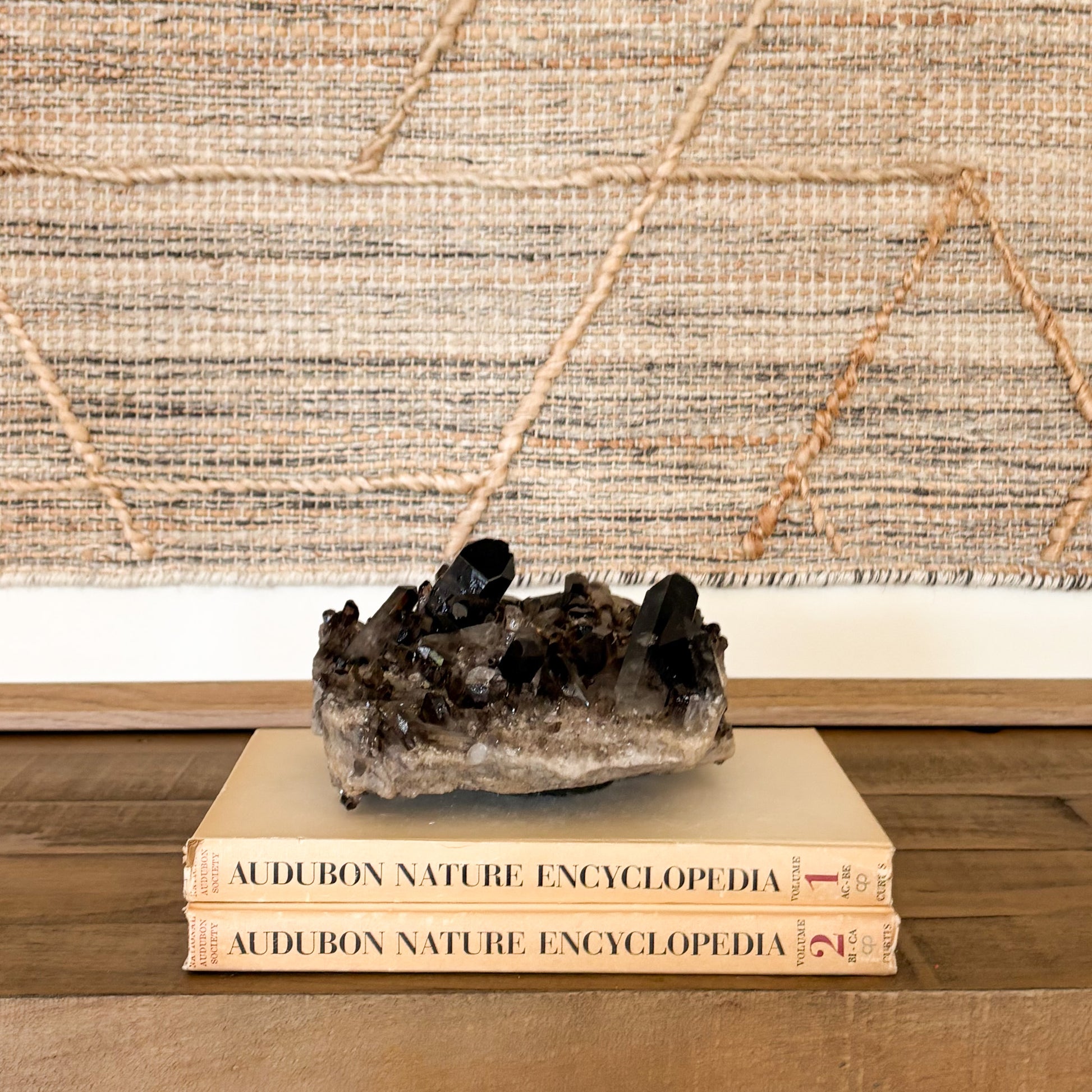 Raw smoky quartz crystal cluster mineral specimen styled on stacked books in a boho home interior.