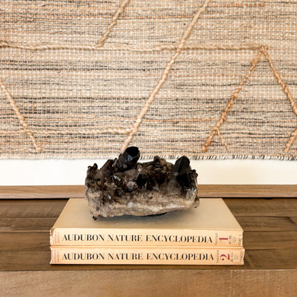 Raw smoky quartz crystal cluster mineral specimen styled on stacked books in a boho home interior.