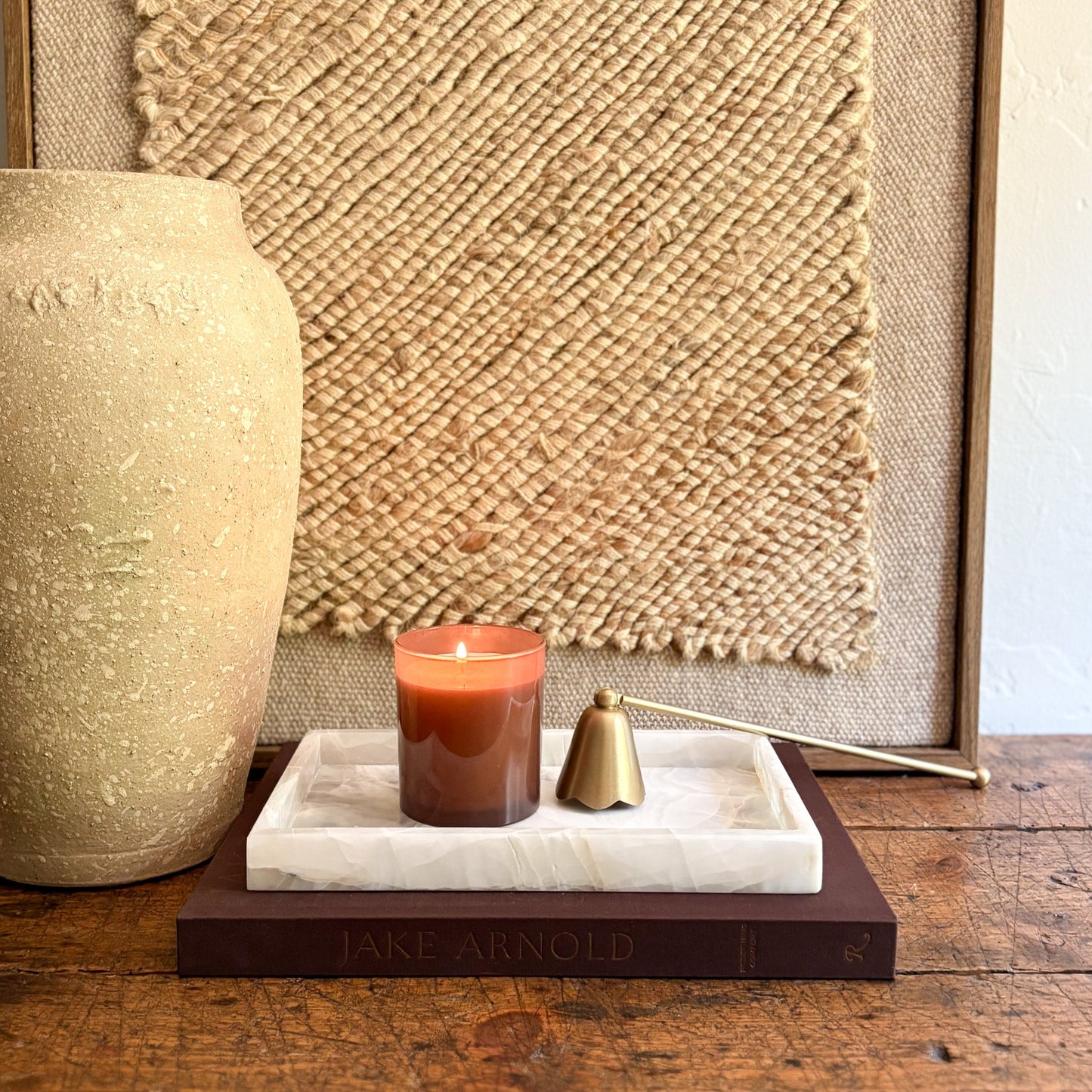 Candle on an onyx tray with a textured wall and vase in the background