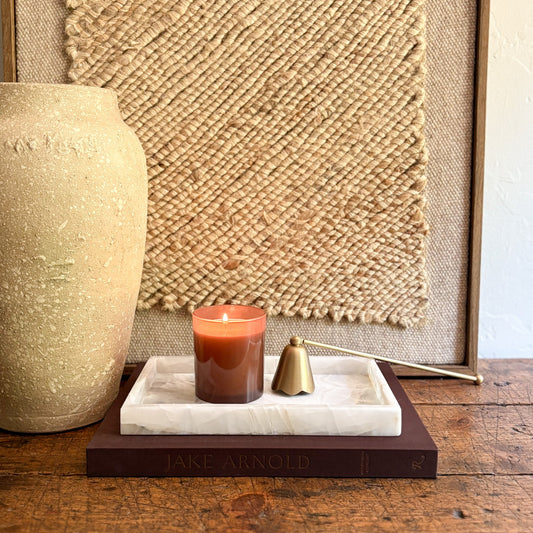 Candle on an onyx tray with a textured wall and vase in the background