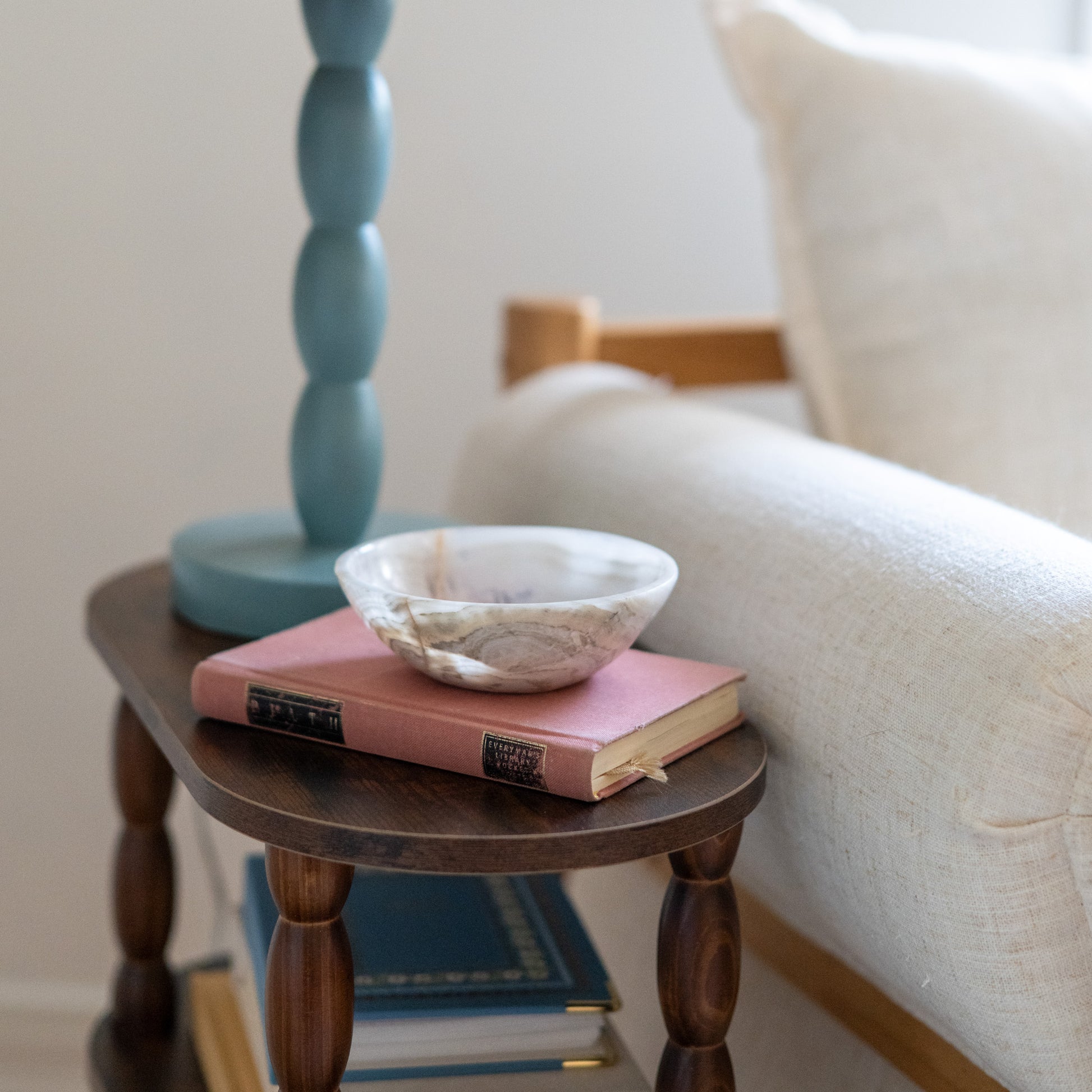 White onyx trinket dish styled on bedside table with vintage book and lamp