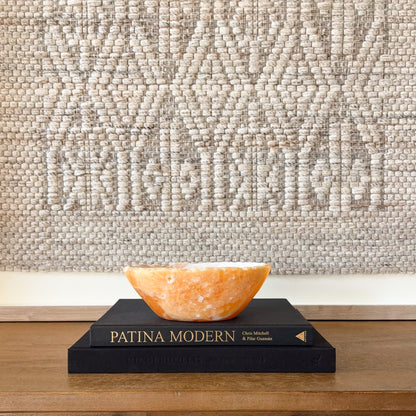 Hand carved zebra calcite bowl with orange honey calcite interior displayed on decorative books for modern home decor