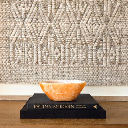 Hand-carved zebra calcite bowl with natural gray veining and orange accents, decorative crystal bowl on books