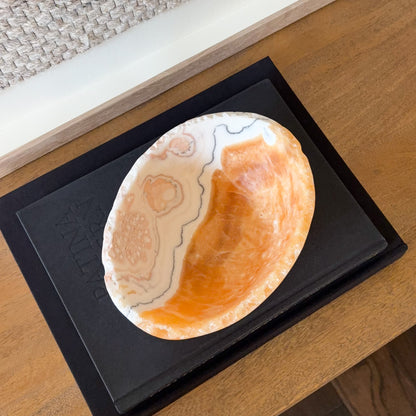 Natural zebra calcite crystal bowl with layered cream, gray, and orange mineral patterns on display books