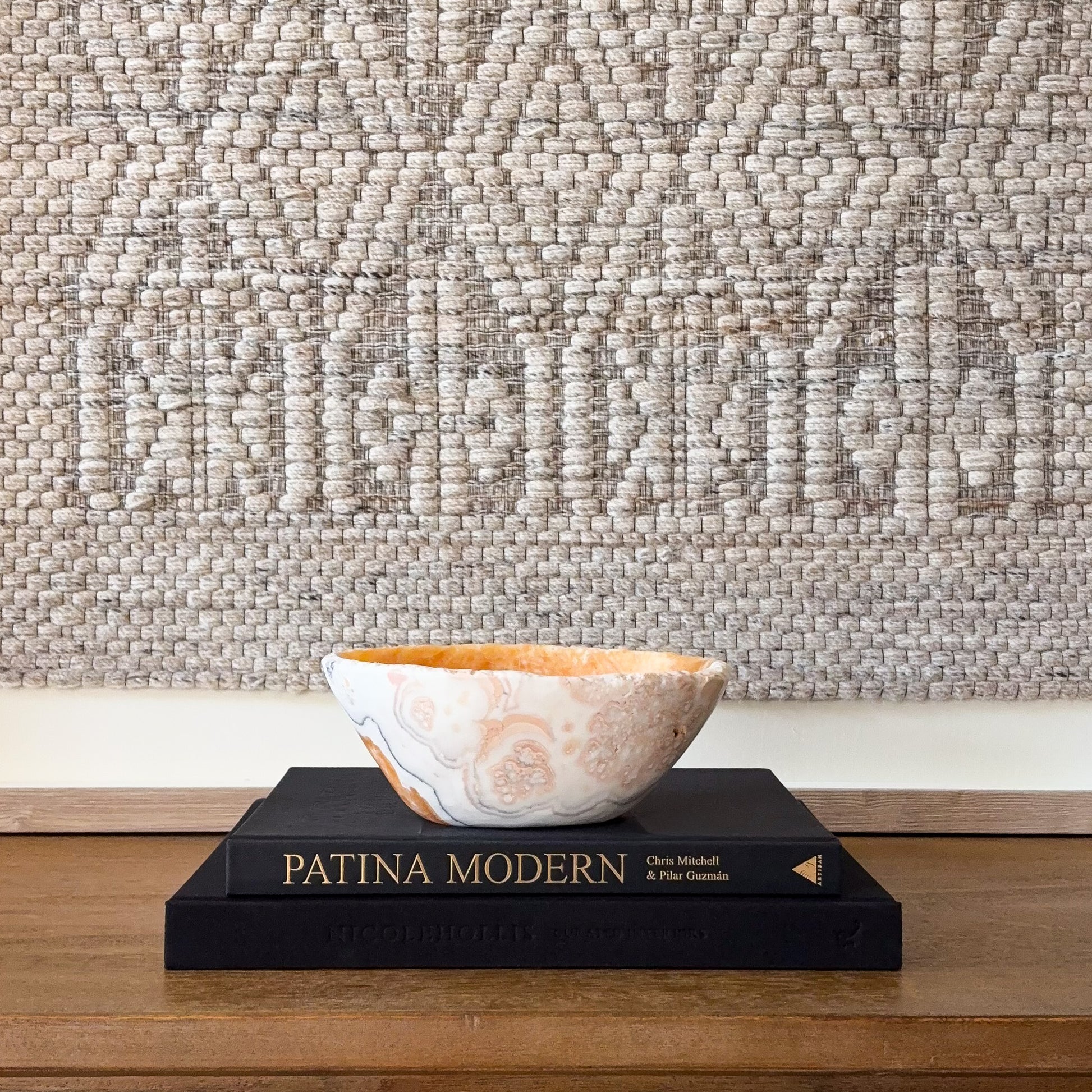 Zebra calcite bowl with cream, gray, and orange banding displayed on stacked books, polished natural stone decor