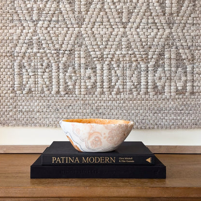 Zebra calcite bowl with cream, gray, and orange banding displayed on stacked books, polished natural stone decor