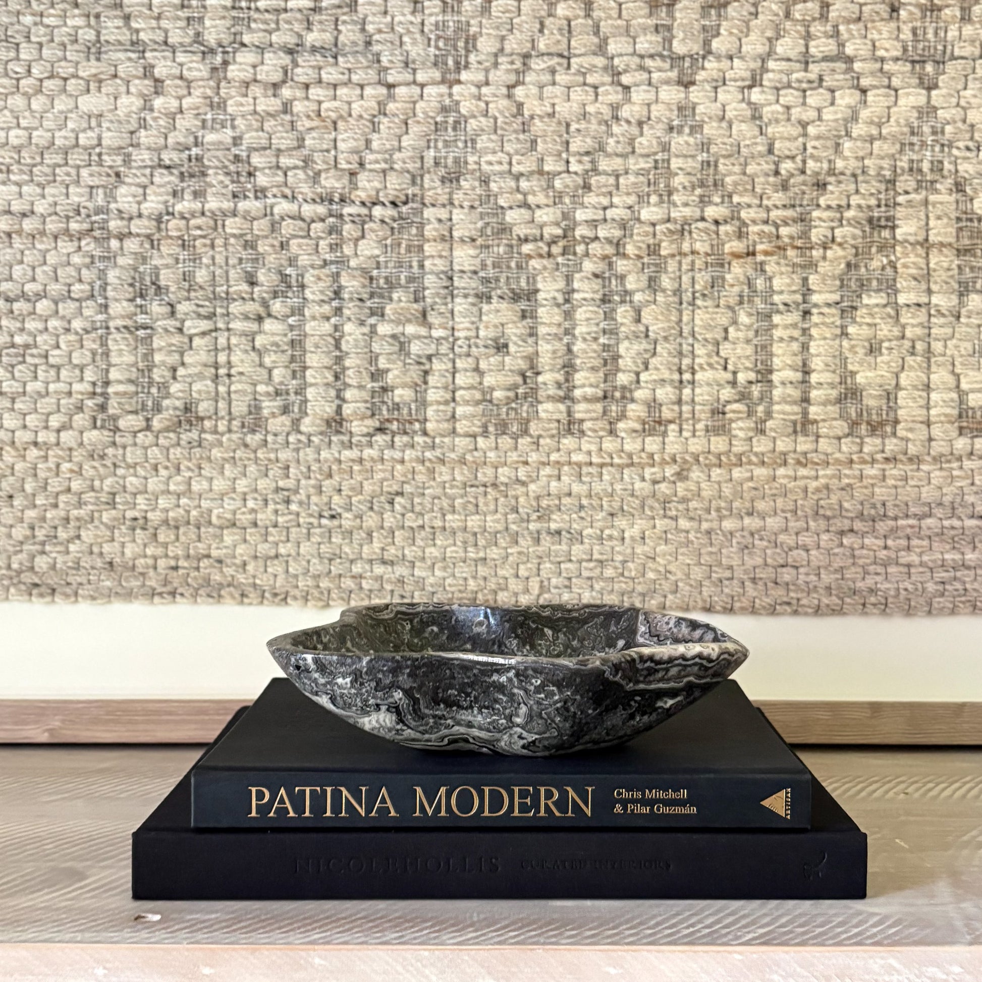 Decorative stone bowl on top of a 'Patina Modern' book with a textured wall background
