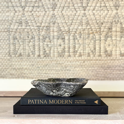 Decorative black and white stone bowl on top of two books titled 'Patina Modern' with a textured wall background.