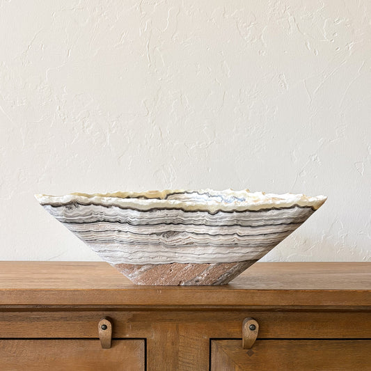 Large striped zebra onyx bowl made from natural stone displayed on wooden cabinet